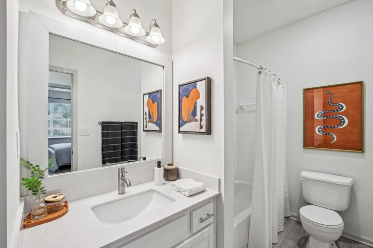 Updated bathroom with white quarts counters, white shaker cabinets, large vanity mirror, hadwood-style flooring, garden style tub with shower and toilet.