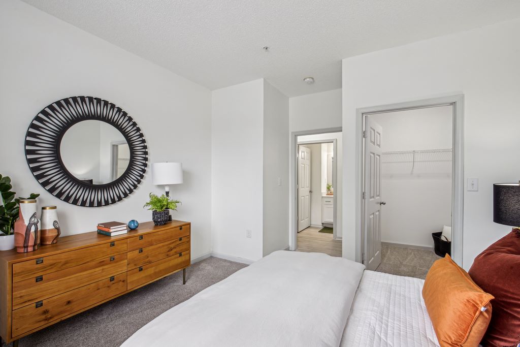 Staged bedroom with bed, dresser, carpeted flooring and walk-in closet.