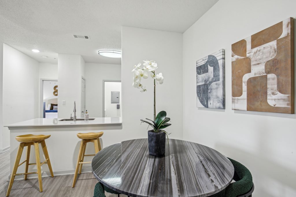 Staged dining room with round table and chairs next to kichen peninsula with two barstools.