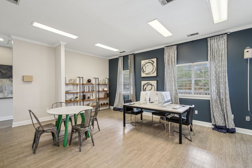 Business center with three computers and chairs, hardwood-style flooring, two windows, and separate table with four chairs.