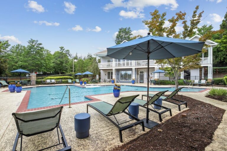 Swimming pool with sundeck and lounge chairs with leasing office in background surrounded by native landscaping.